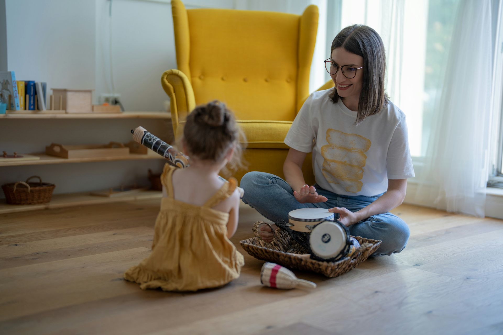 A woman is sitting on the floor playing drums with a little girl.