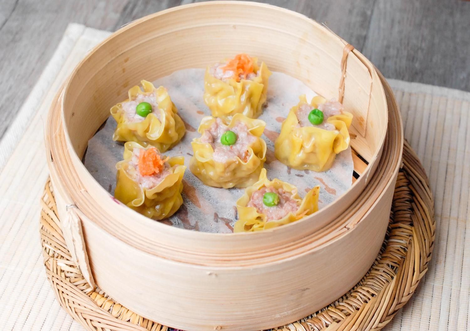 Steamed dumplings in a bamboo basket on a woven placemat