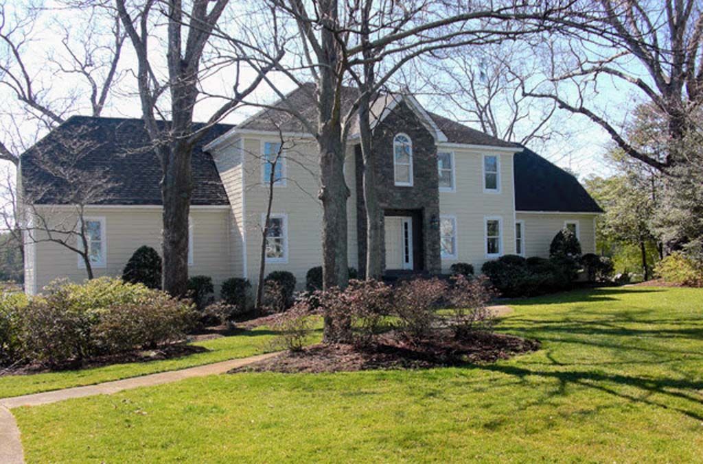 A large white house with a black roof is surrounded by trees and grass.