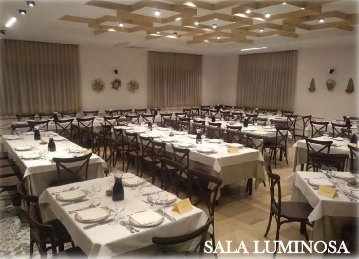 Tavoli rotondi con tovaglie, copri sedie di color bianco e un'aiuola al centro con delle palme