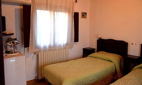 Una stanza con due letti singoli, aria condizionata al muro e una mensola con un Tv