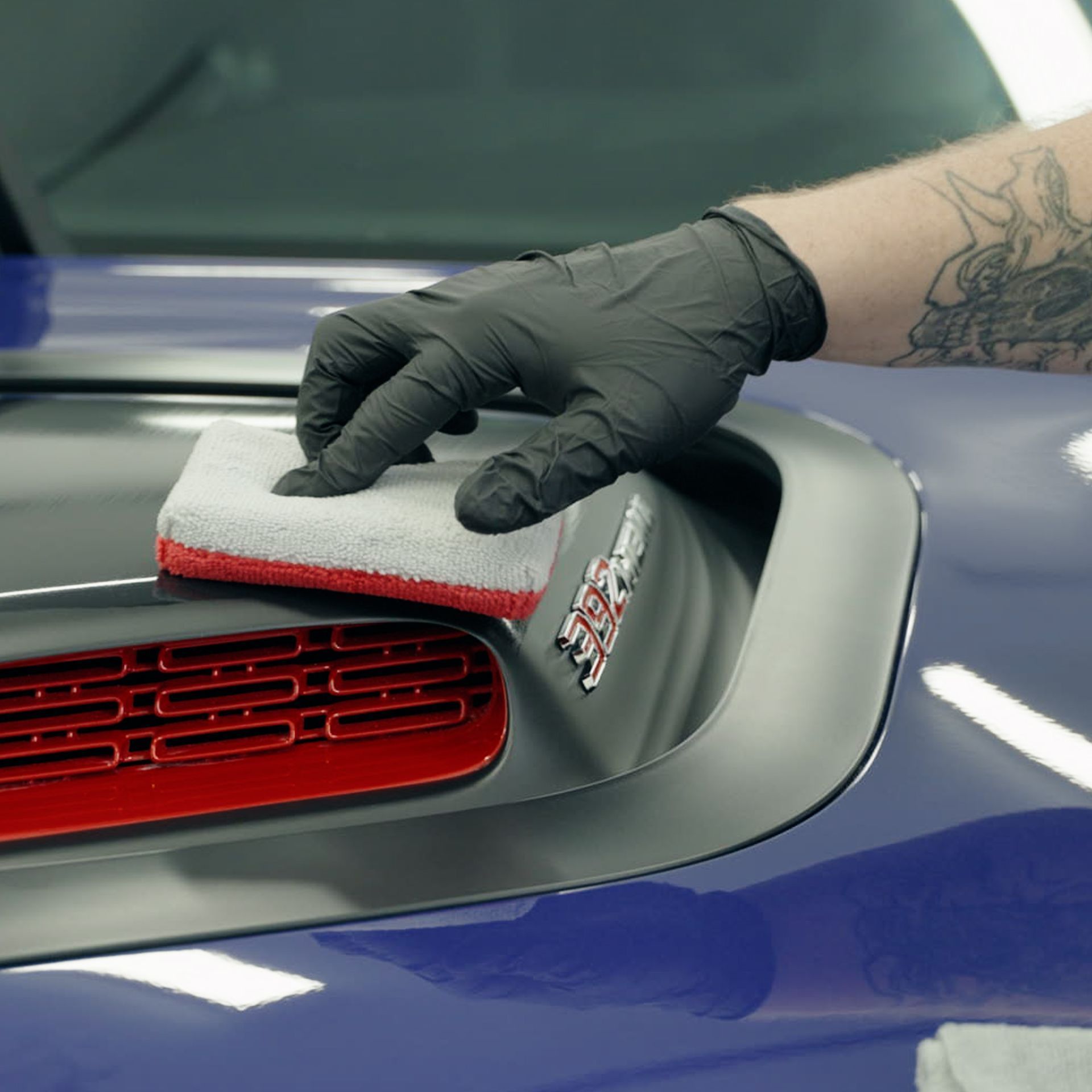 A person wearing black gloves is cleaning the hood of a blue car
