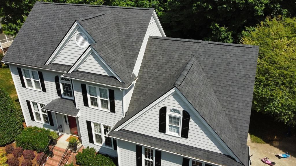 An aerial view of a large white clean  house with a gray roof and black shutters.