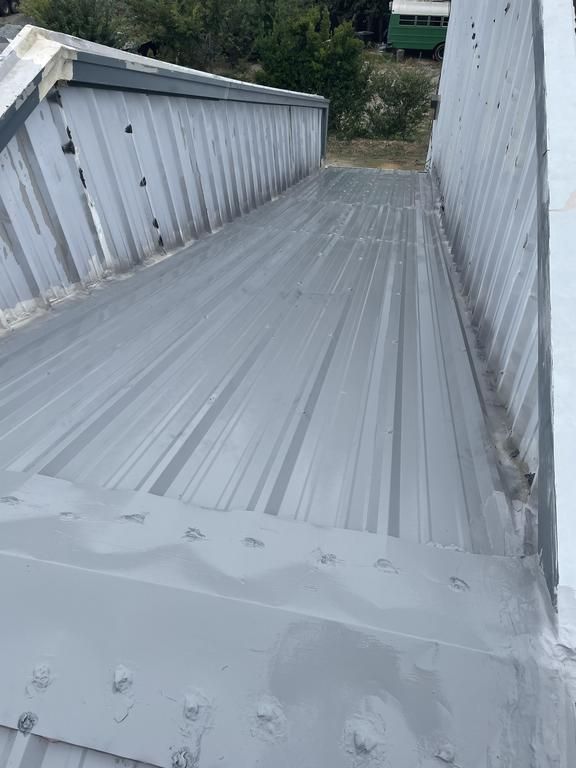 A gray metal roof with a green building in the background.