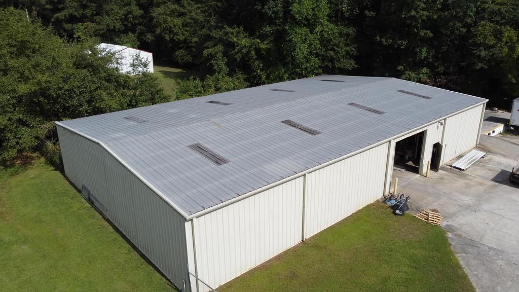 An aerial view of a large white building with a metal roof surrounded by trees.