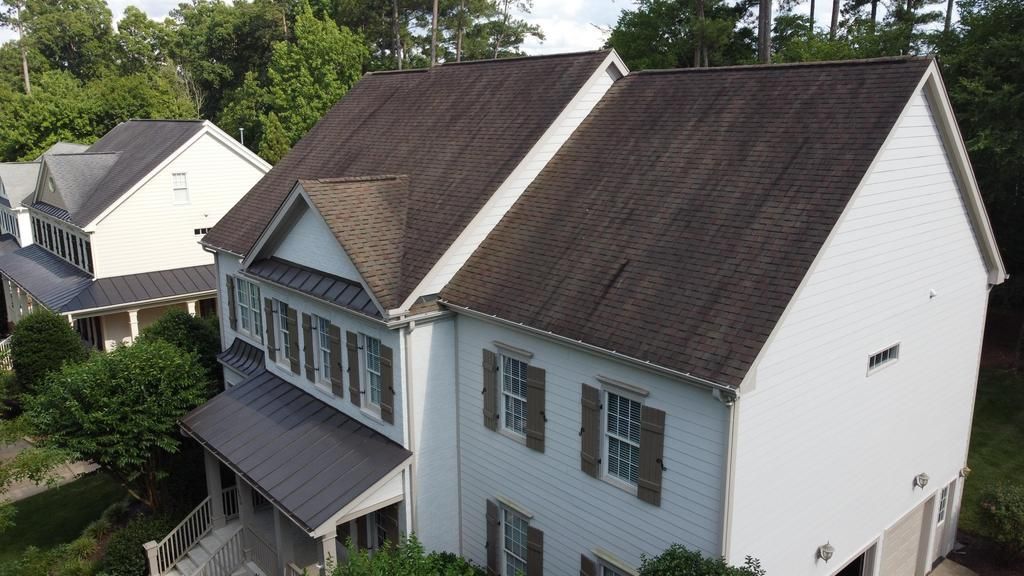 An aerial view of a white house with a brown roof surrounded by trees.