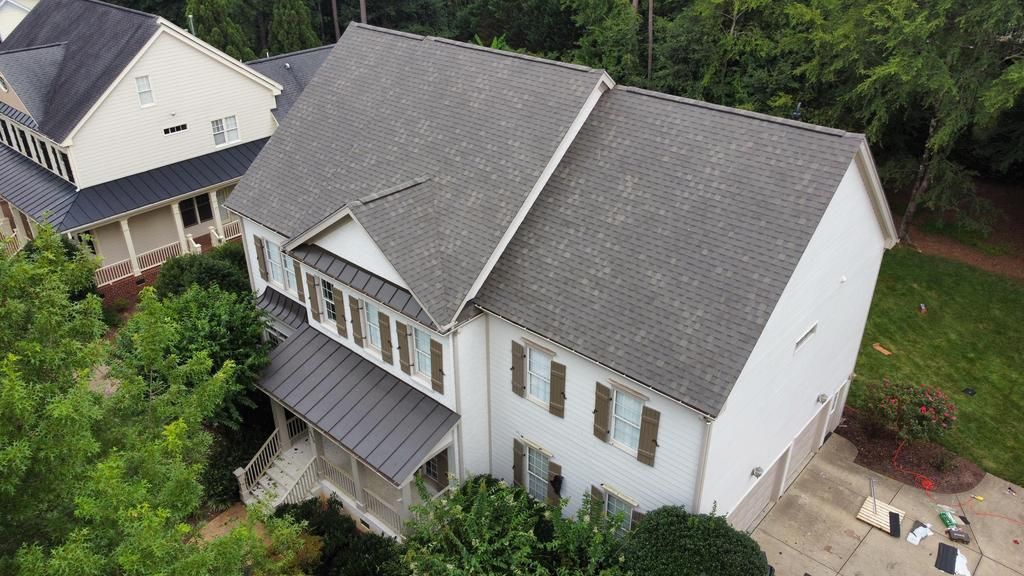 An aerial view of a large clean white house with a gray roof surrounded by trees.