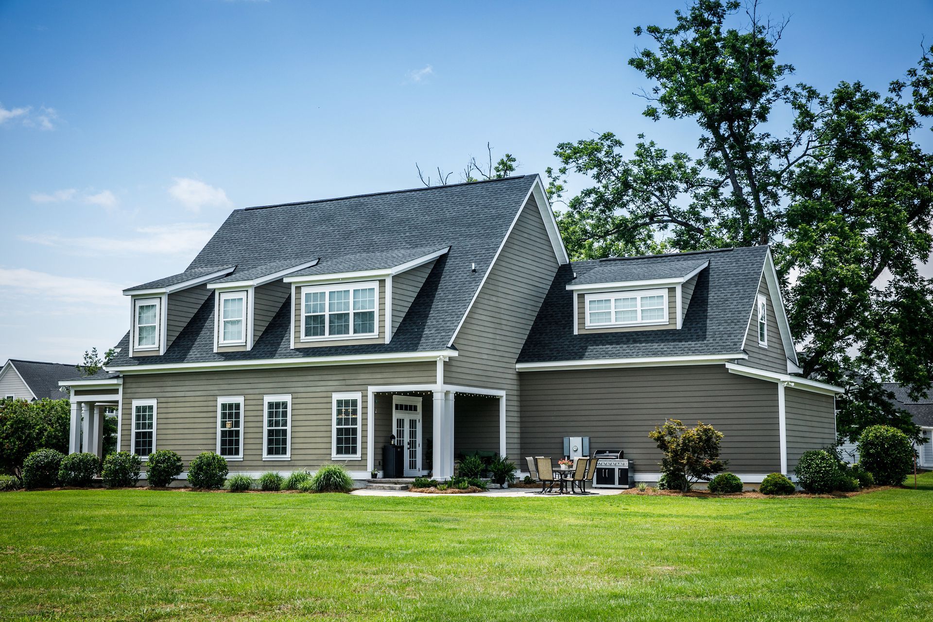 Two-story house with gray siding, dark roof, multiple windows, and dormers on a green lawn.