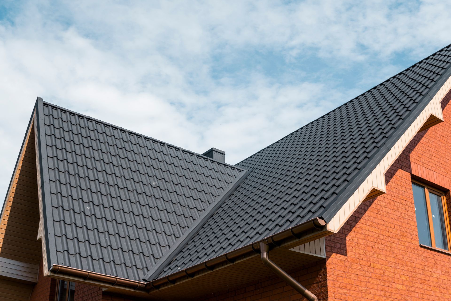 Black metal roof on a red brick house against a cloudy sky.