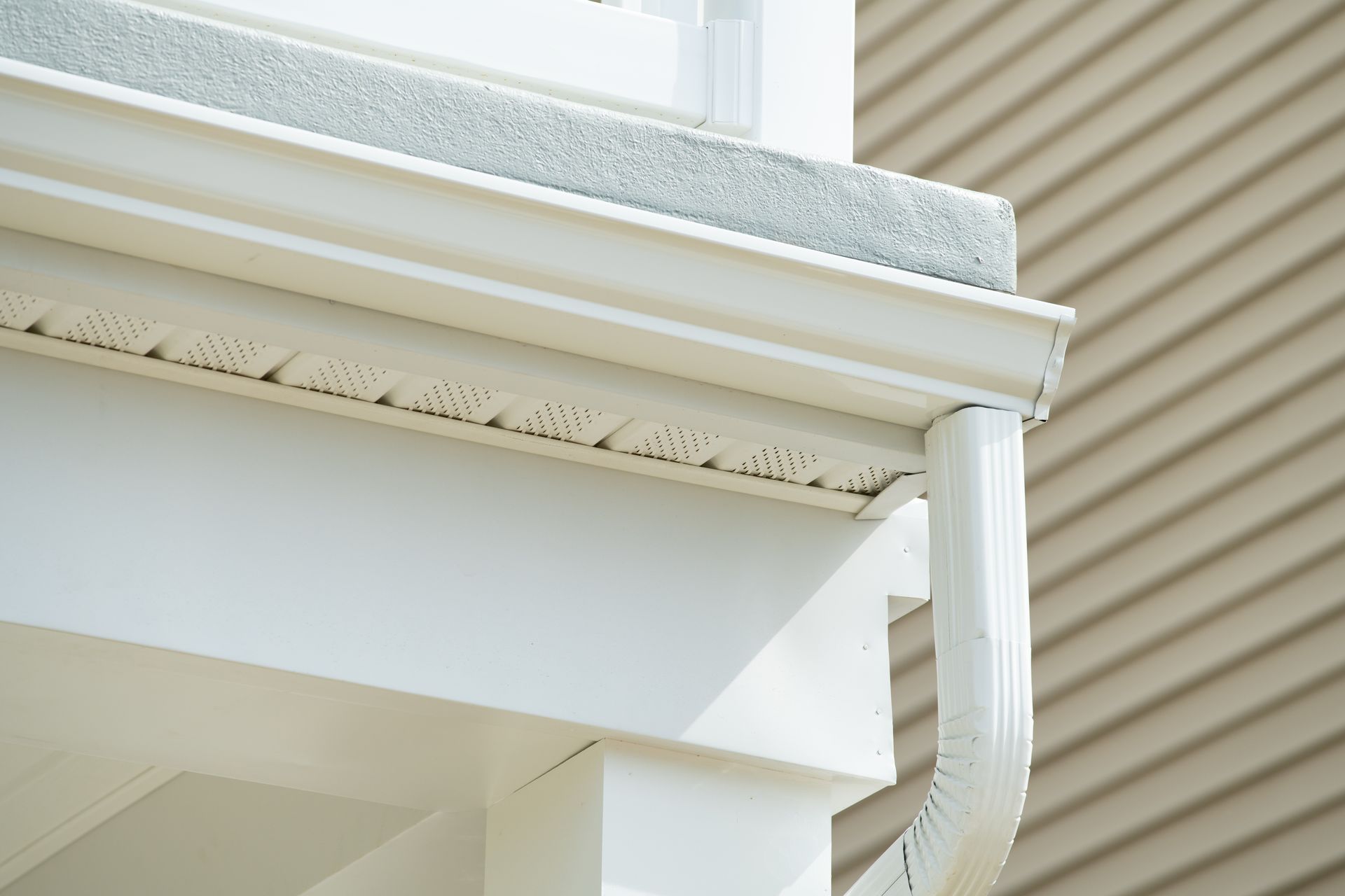 White rain gutter and downspout on a white building with beige siding.