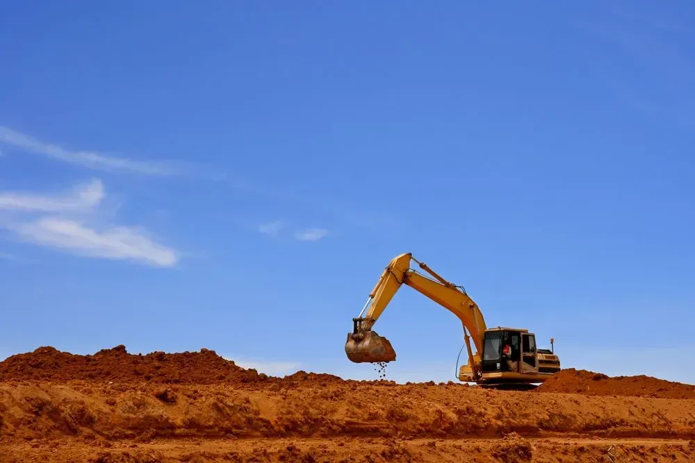 A Yellow Excavator Works on a Site With Mounds of Reddish-brown Soil — Copp & Co Civil Plant Hire in Mount Julian, QLD