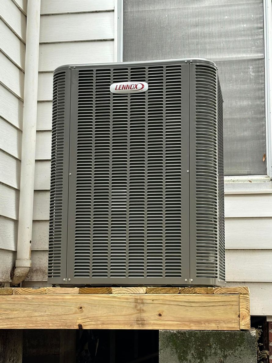Air conditioning unit mounted on a wooden platform against a white house wall.