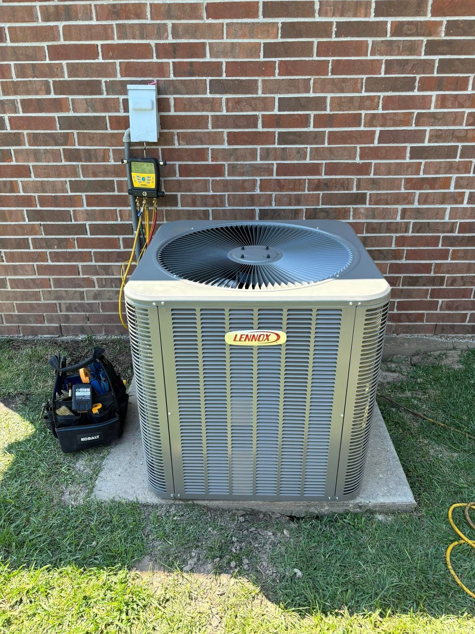 An air conditioning unit against a brick wall, with tools and a power box.