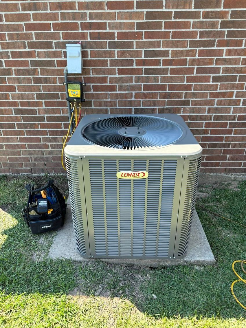 An air conditioning unit against a brick wall, with tools and a power box.