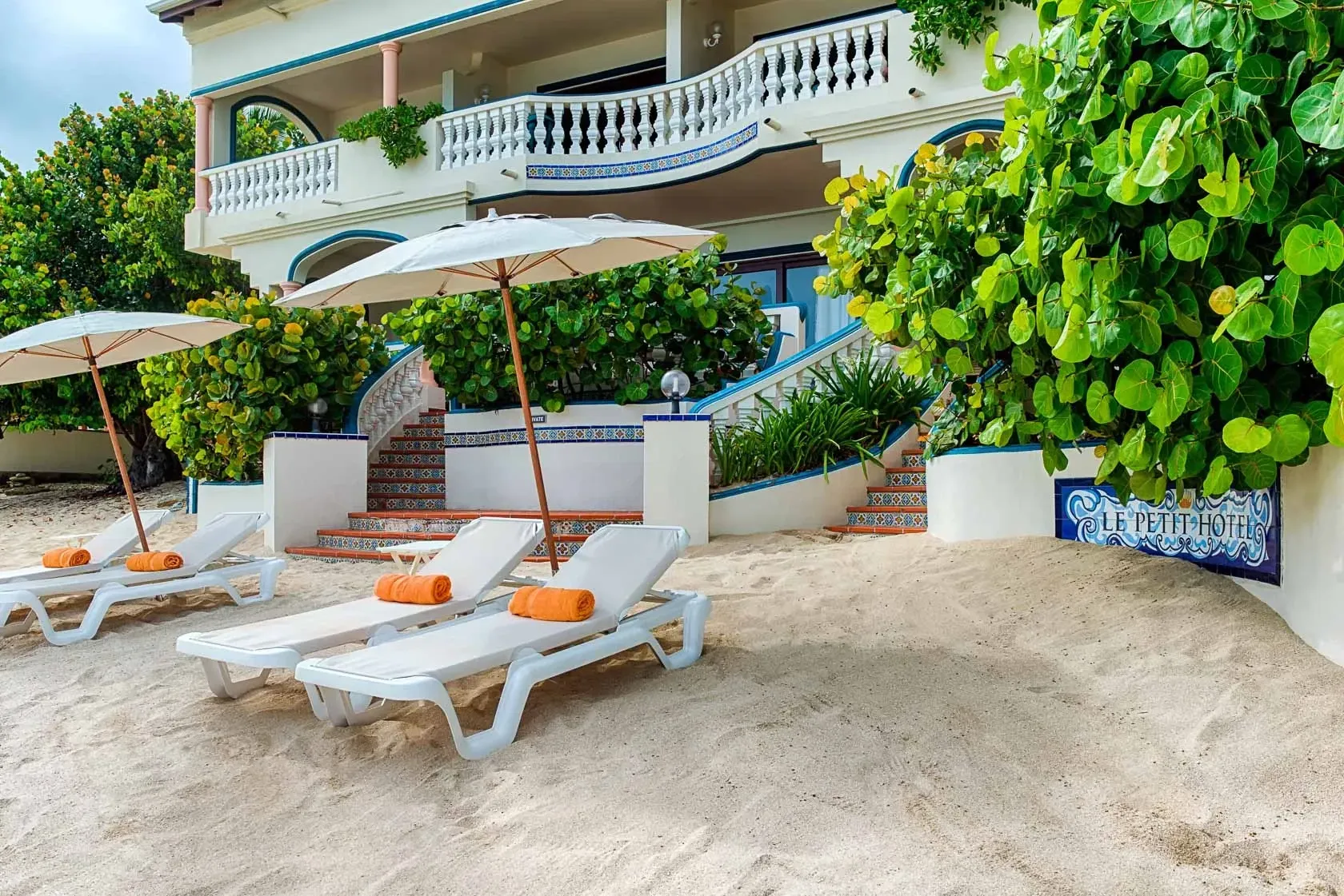 Beachfront villa with lounge chairs, umbrellas, and lush greenery.