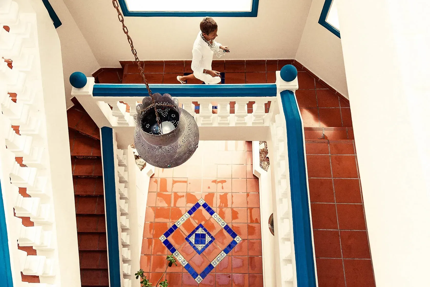 Boy jumps down stairs, in a building with white and blue railings.