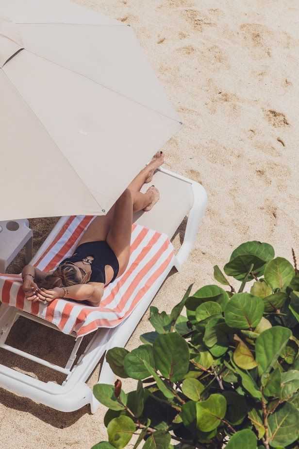 Woman in black swimsuit sunbathing on a striped beach chair under an umbrella.