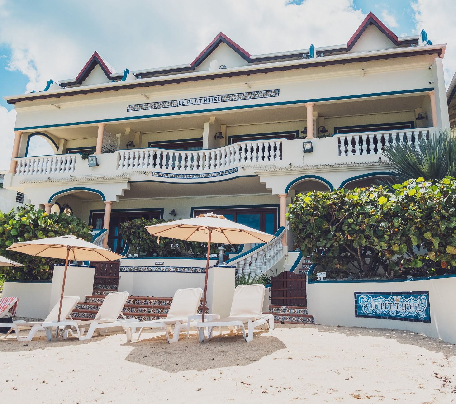 Beachfront resort with white facade, balconies, beach chairs, and umbrellas.