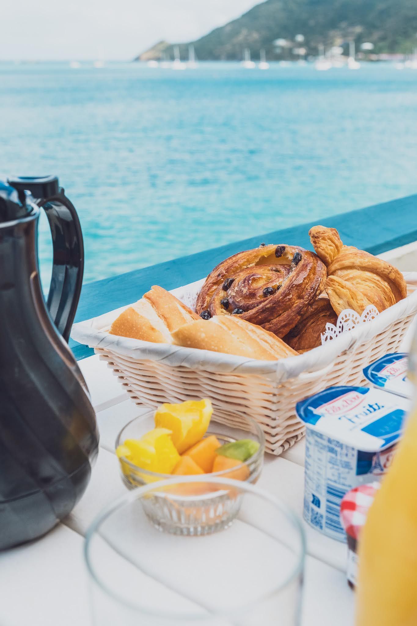 Breakfast basket with pastries, fruit, and yogurt on a table overlooking the ocean.