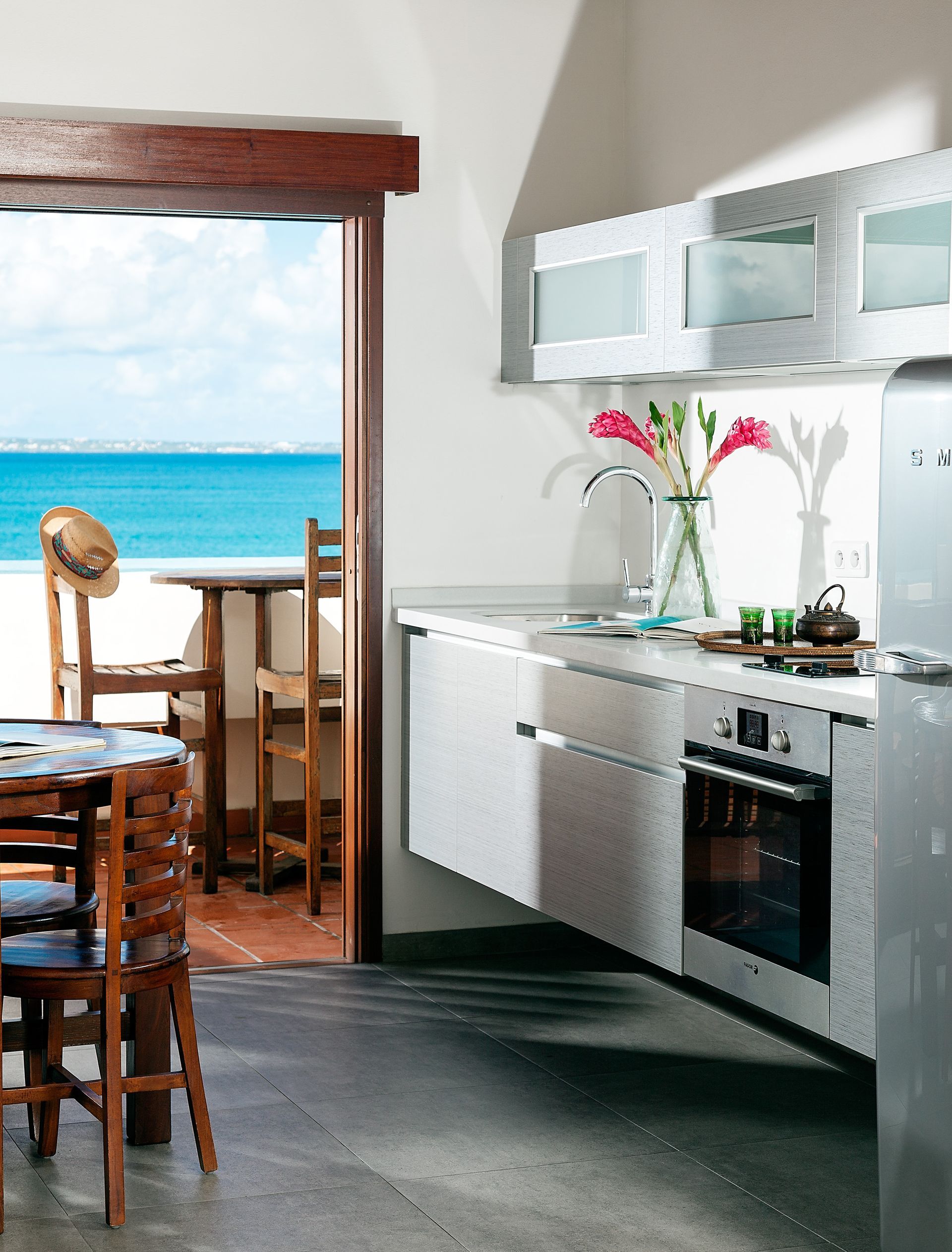 Kitchen with stainless steel appliances, open to beach view, chairs, and hat.