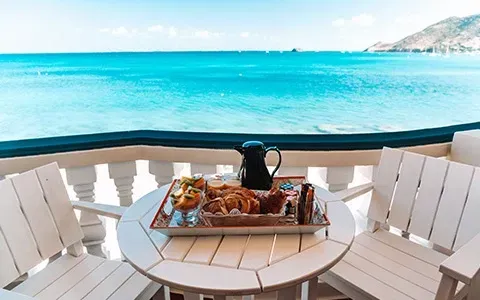 Breakfast tray on a white table overlooking a turquoise ocean from a balcony.