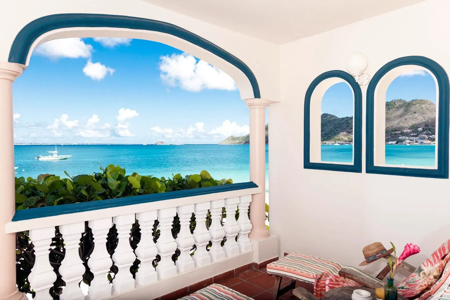 Balcony overlooking turquoise ocean; white railing, blue trim, sunny day.