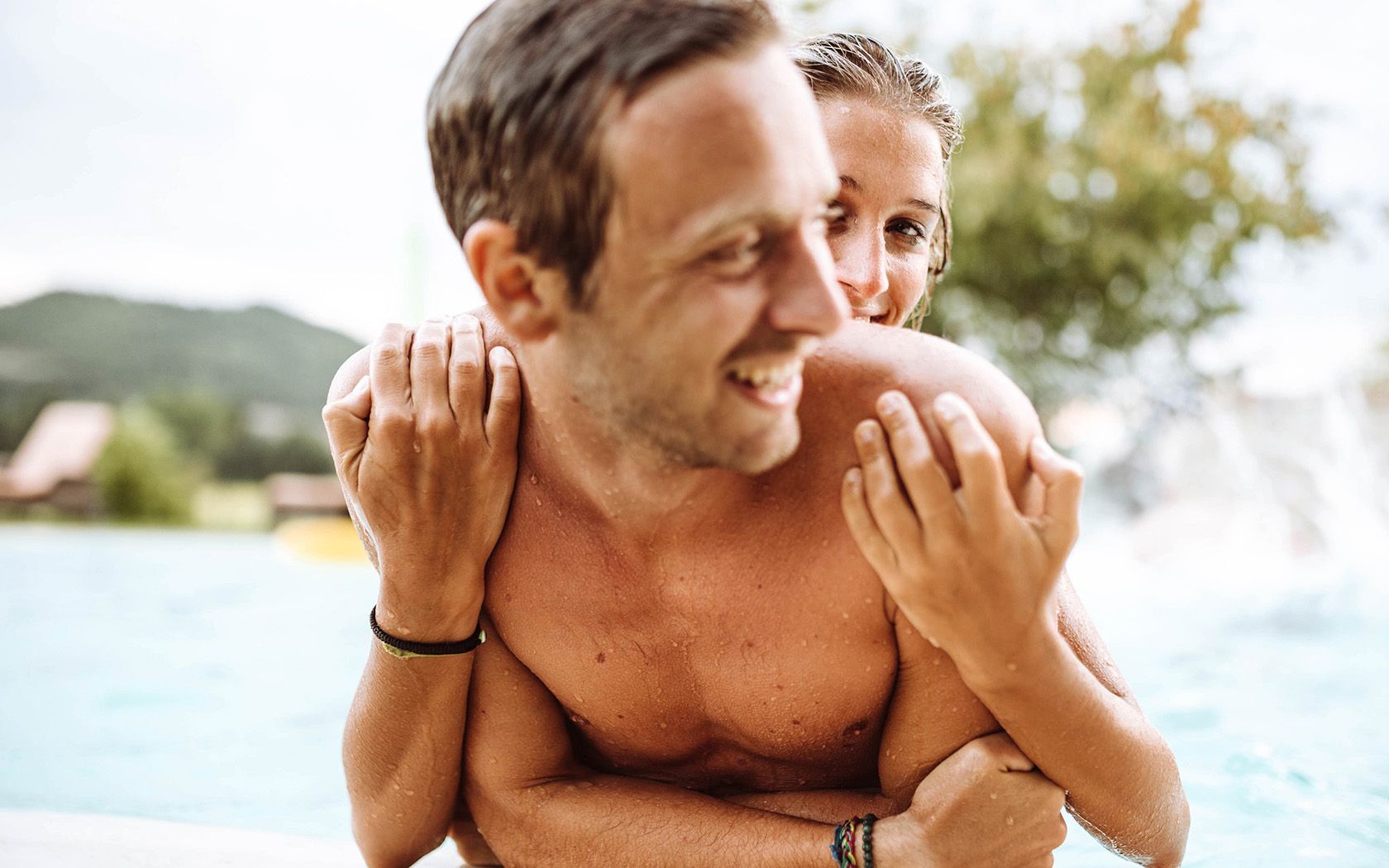 Man giving woman a piggyback ride in a pool. Both are smiling.