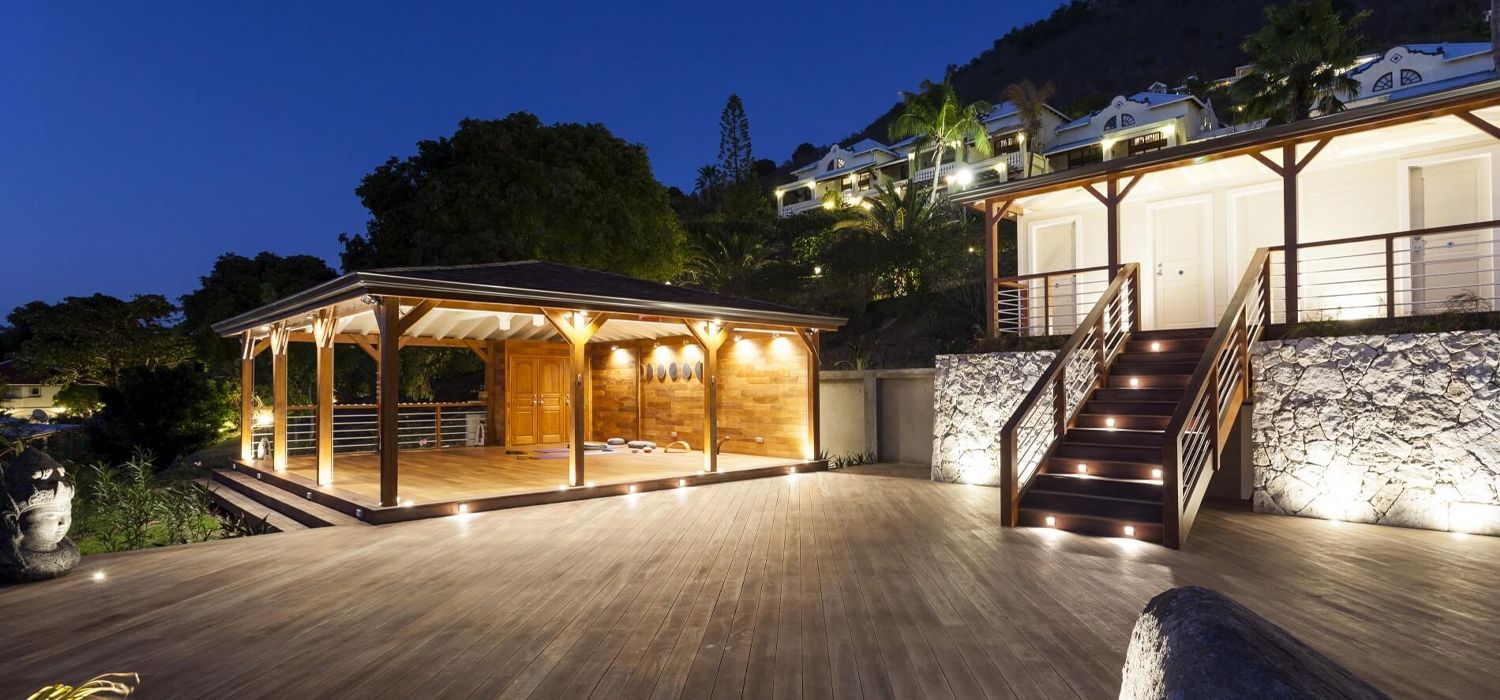 Wooden structures on a deck, illuminated at night. Steps lead up to a building with rock wall.