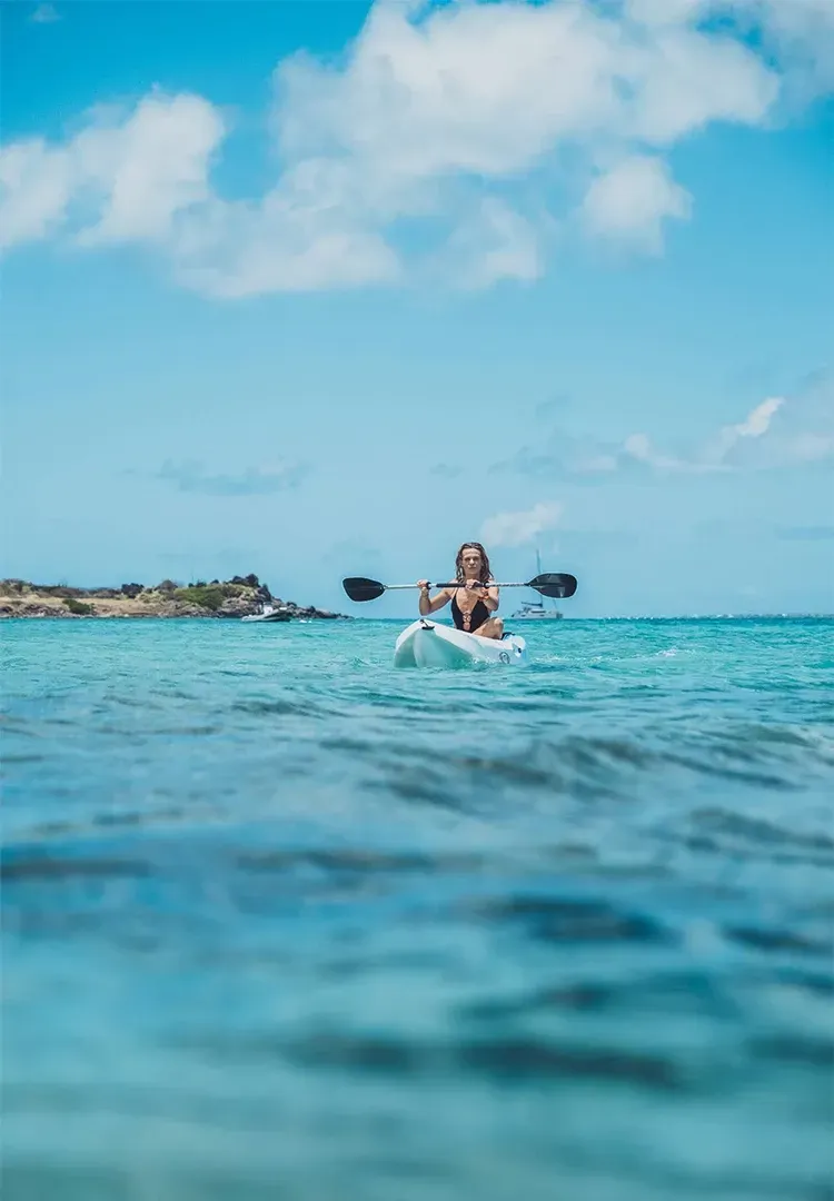 Woman kayaking on turquoise water under a blue sky with clouds.