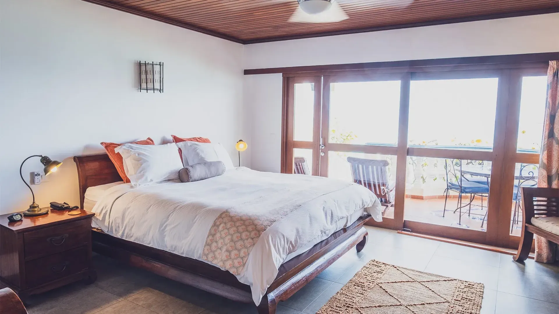 Bedroom with a bed, nightstand, balcony access via glass doors, and wooden ceiling.