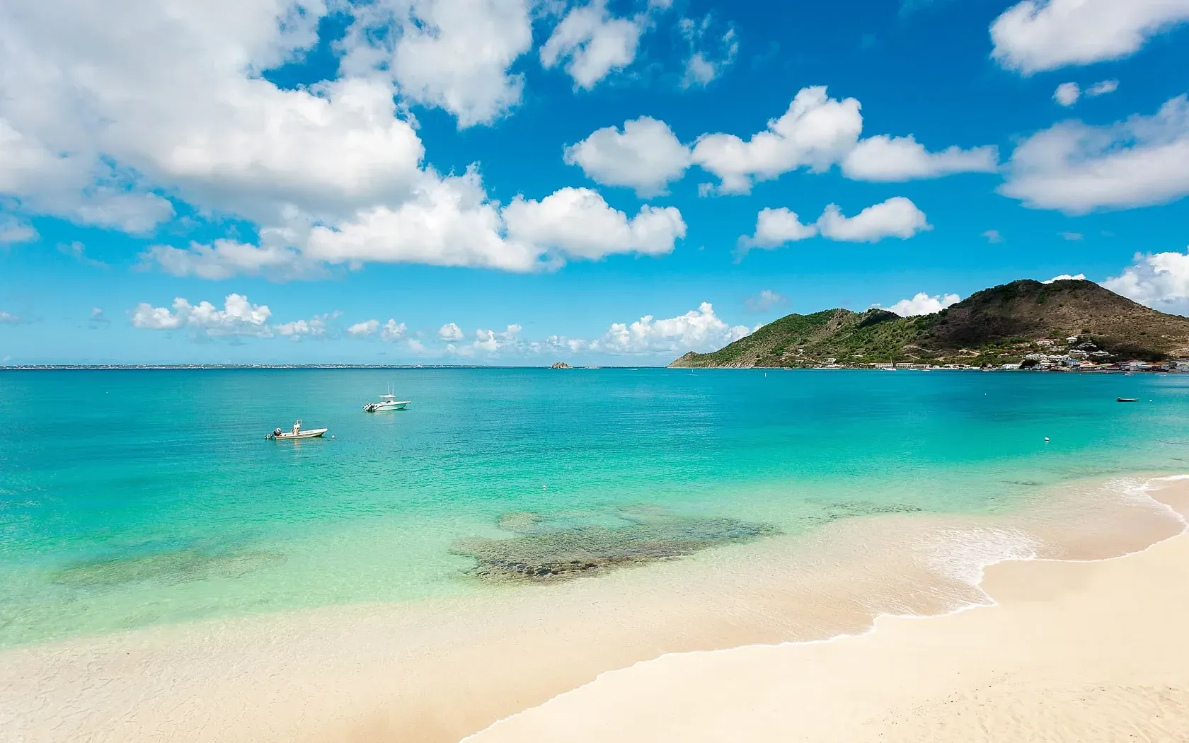Beach with turquoise water, white sand, blue sky with clouds, and a distant island.
