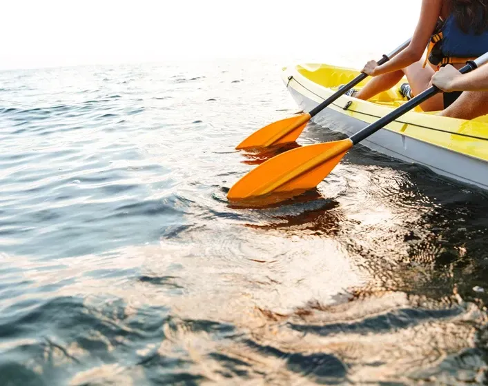 Two people kayaking on blue water with orange paddles.