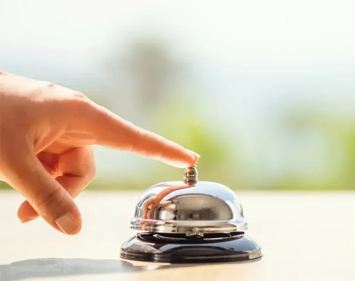 Hand presses a silver bell on a wooden surface, outdoors, blurred background.