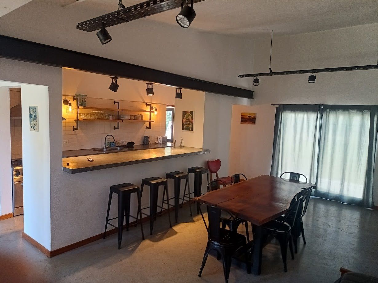 Cocina/comedor abierto con barra, taburetes y una mesa de madera con sillas cerca de puertas corredizas de vidrio.