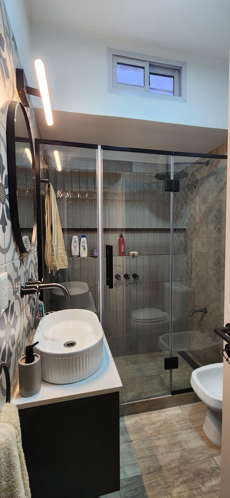 Baño moderno con ducha de cristal, lavabo flotante y azulejos con dibujos decorativos.