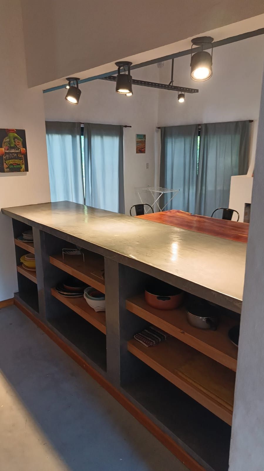 Isla de cocina con encimera de hormigón, estantes abiertos e iluminación de riel.