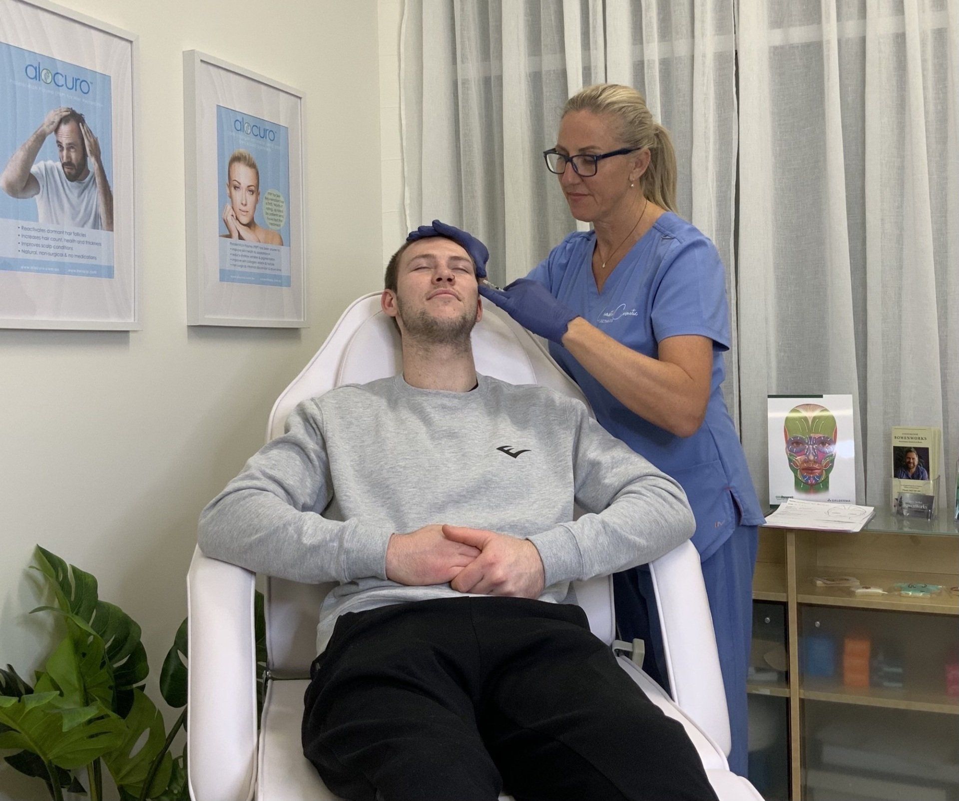 A man is sitting in a chair with his eyes closed while a nurse examines his head