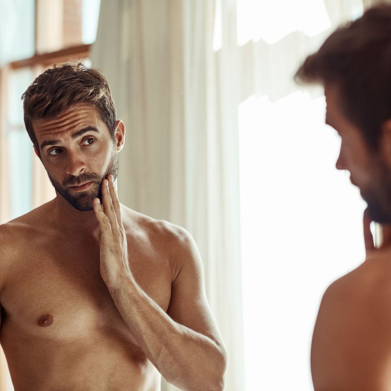 A shirtless man is looking at himself in the mirror.