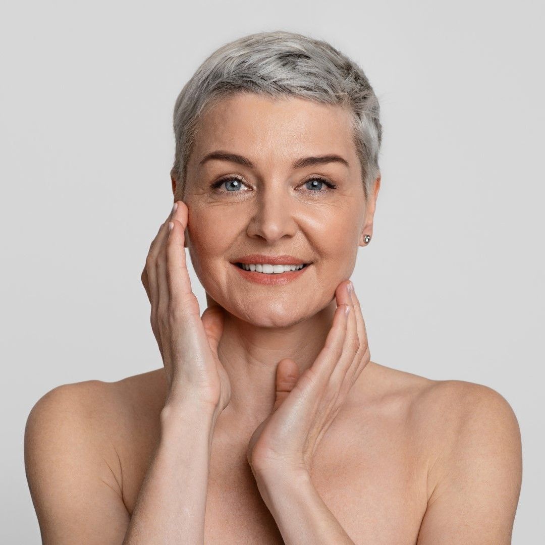 A woman with short hair is smiling and touching her face with her hands.