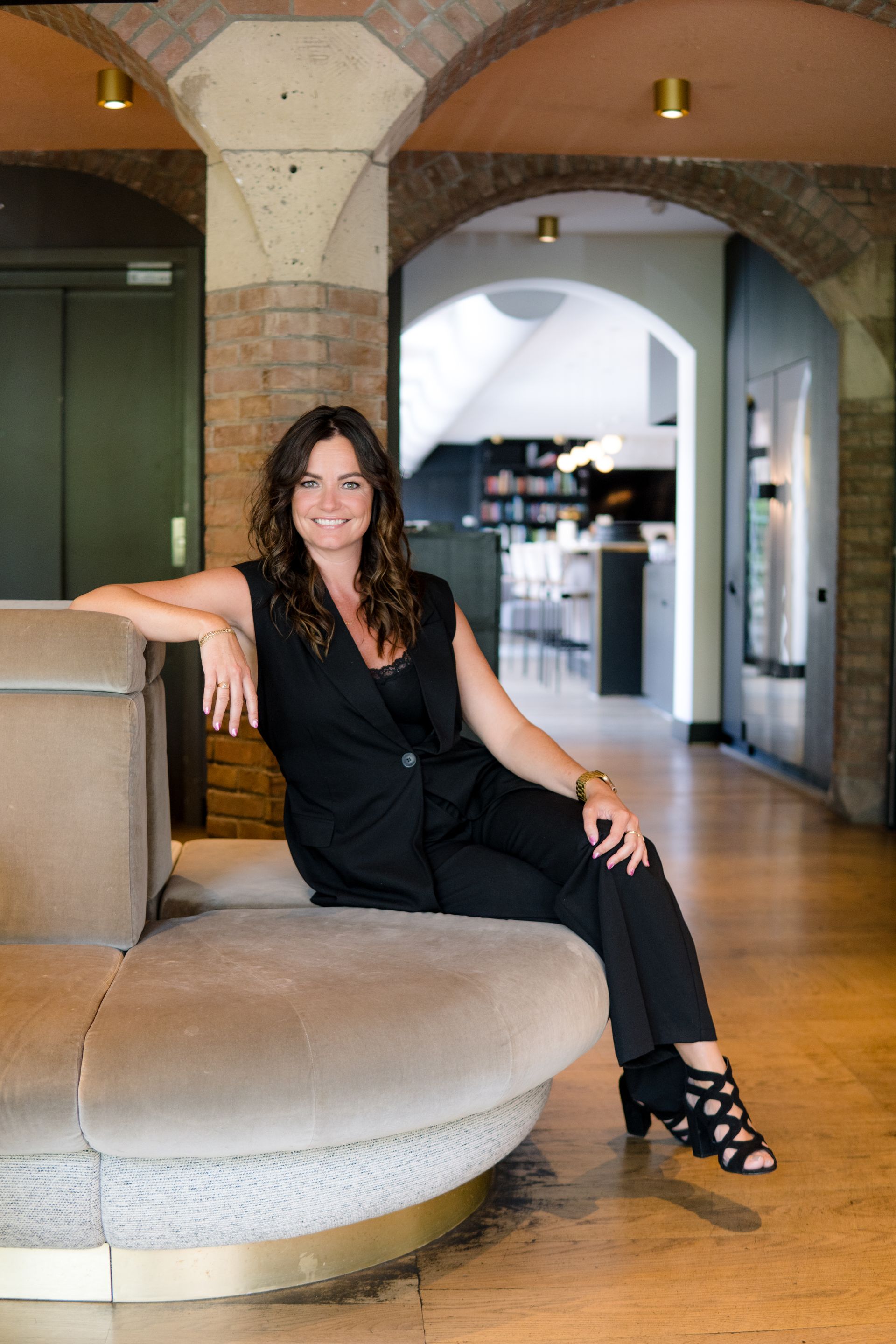 Een persoon zit glimlachend op stenen trappen voor twee donkere deuren met het opschrift