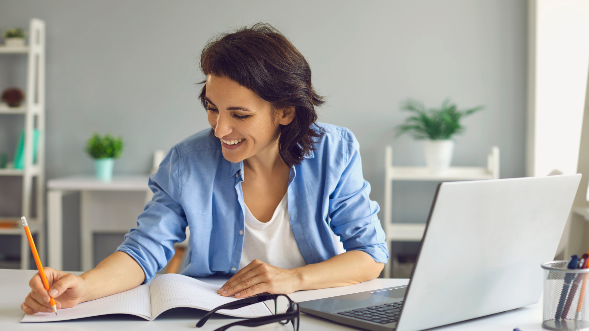 A woman is sitting at a desk with a laptop and a notebook.