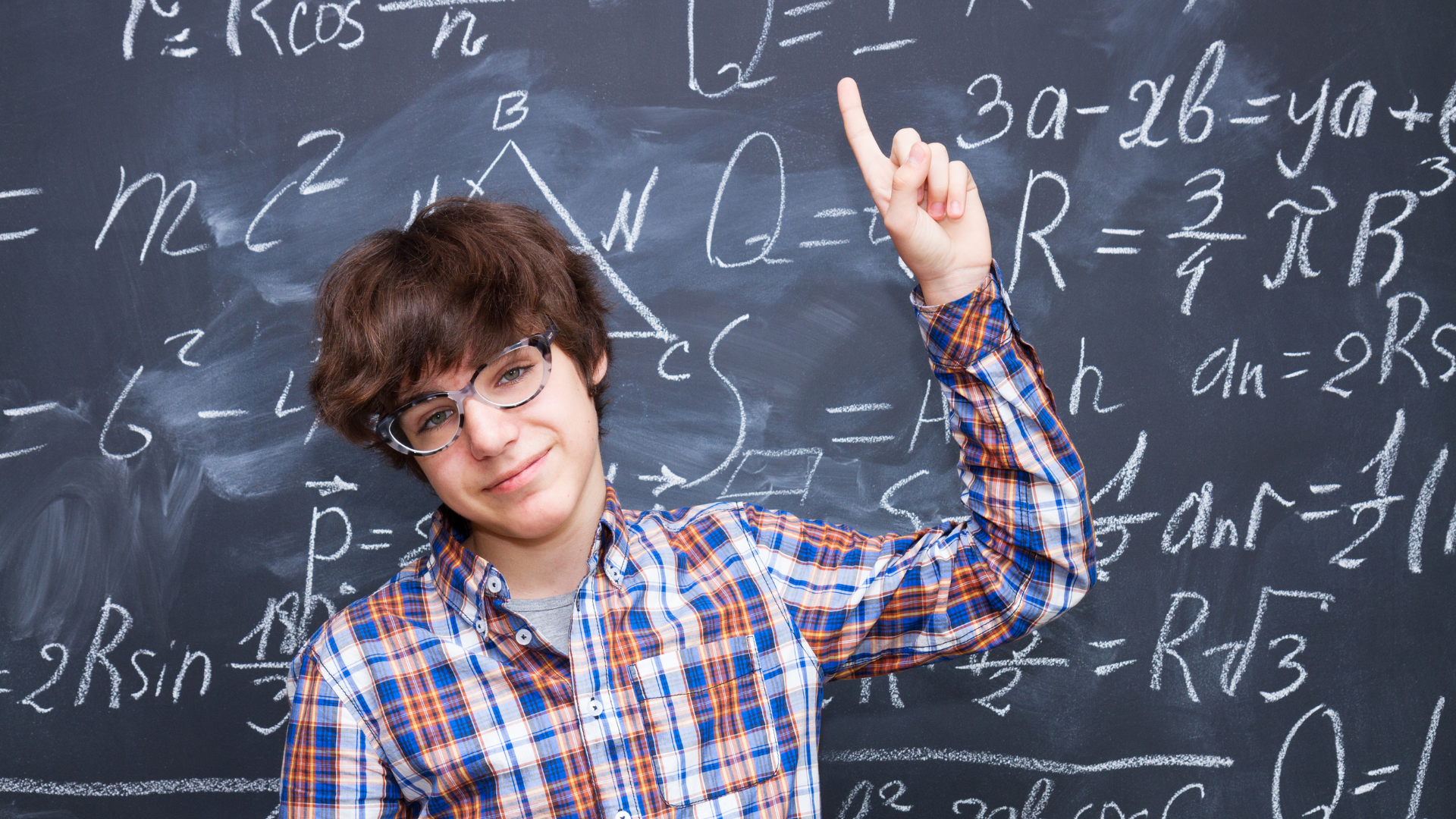 A young man is standing in front of a blackboard with math equations on it.