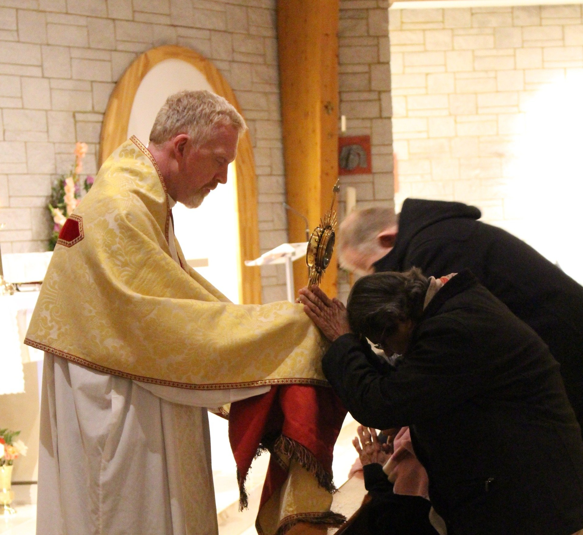 priest in a yellow robe is praying with a woman in a black coat