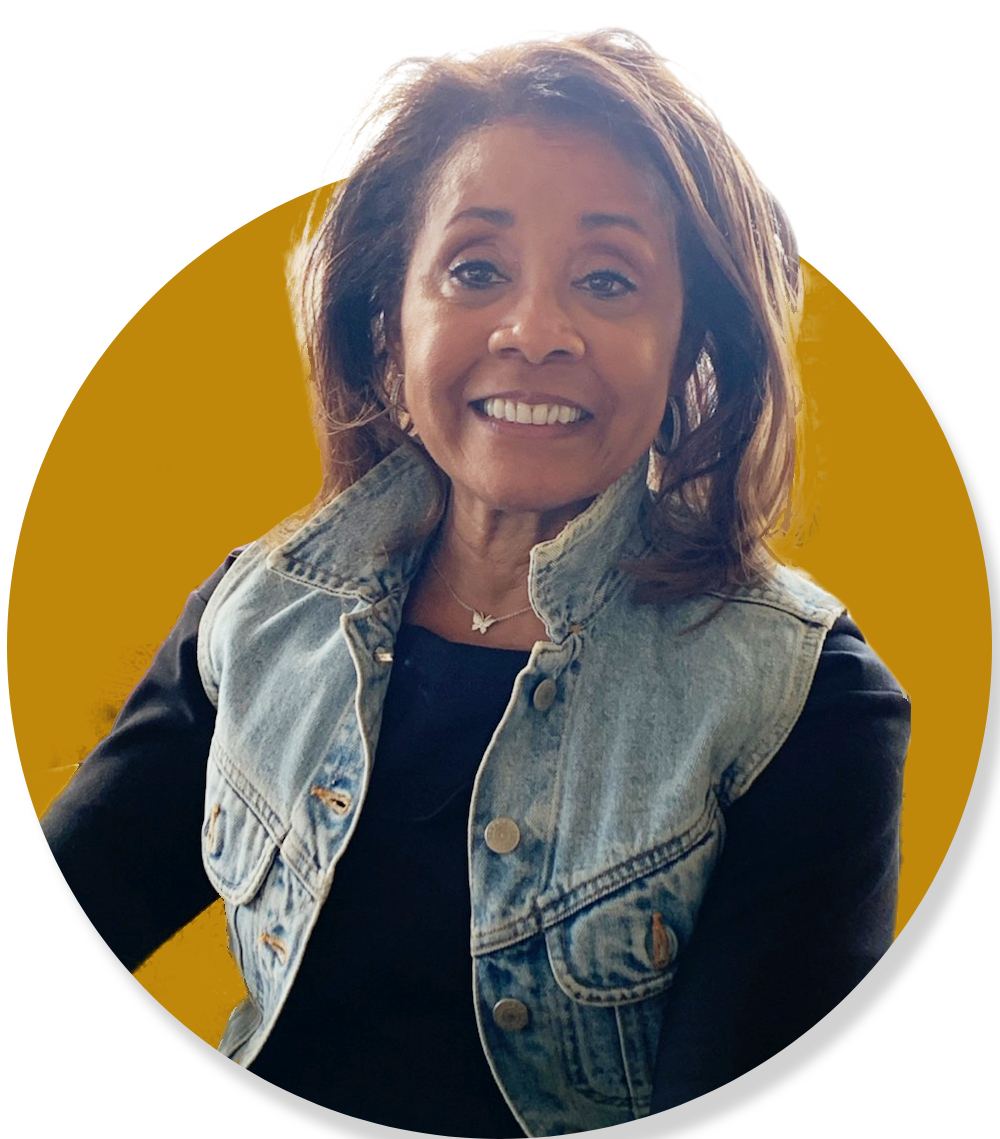 Diane wearing a black shirt and a denim vest smiles for the camera