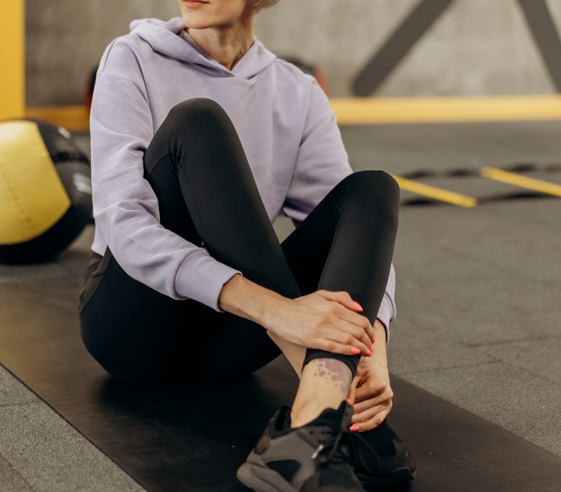 A woman is sitting on a yoga mat in a gym.
