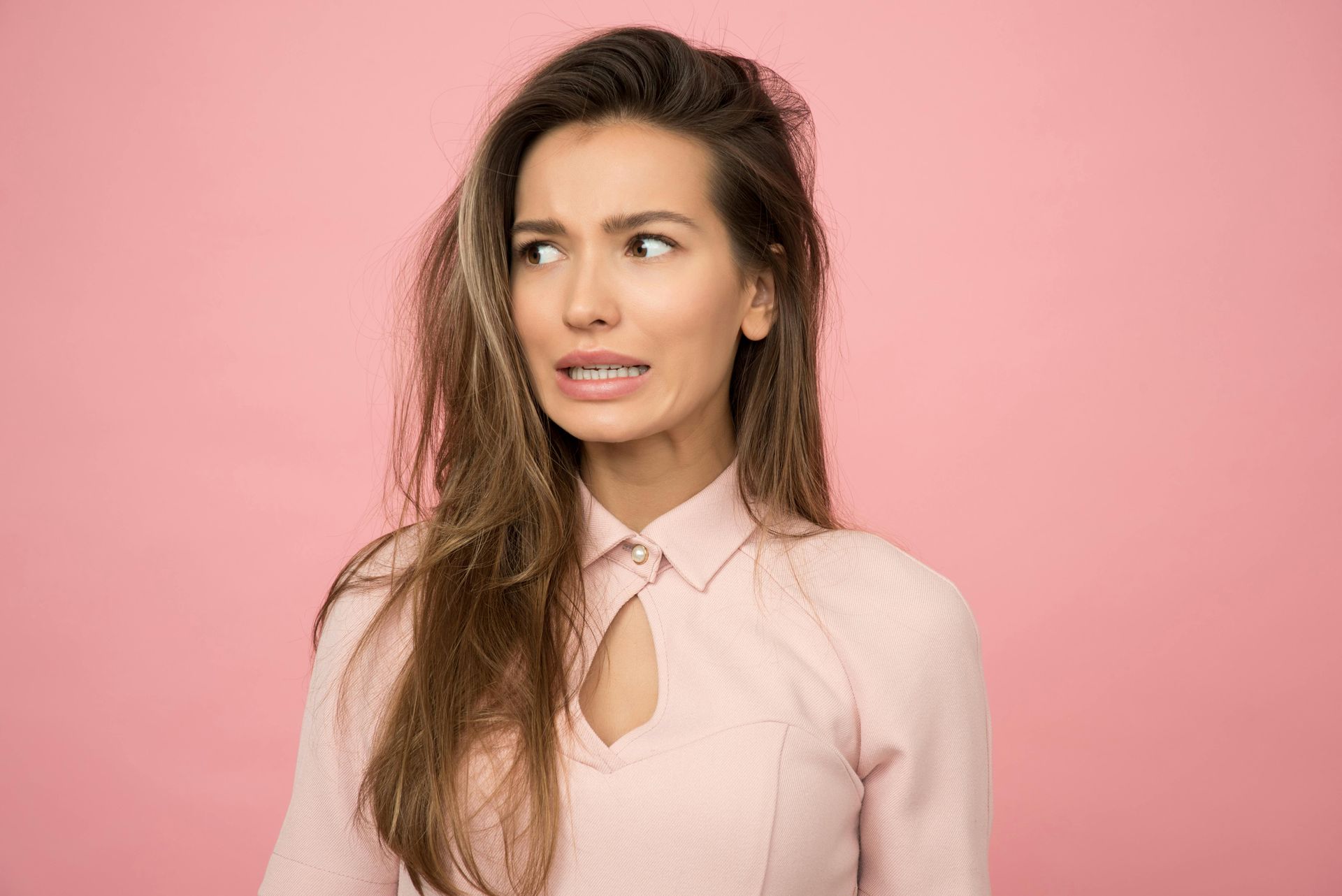 A woman with long hair is making a funny face on a pink background.