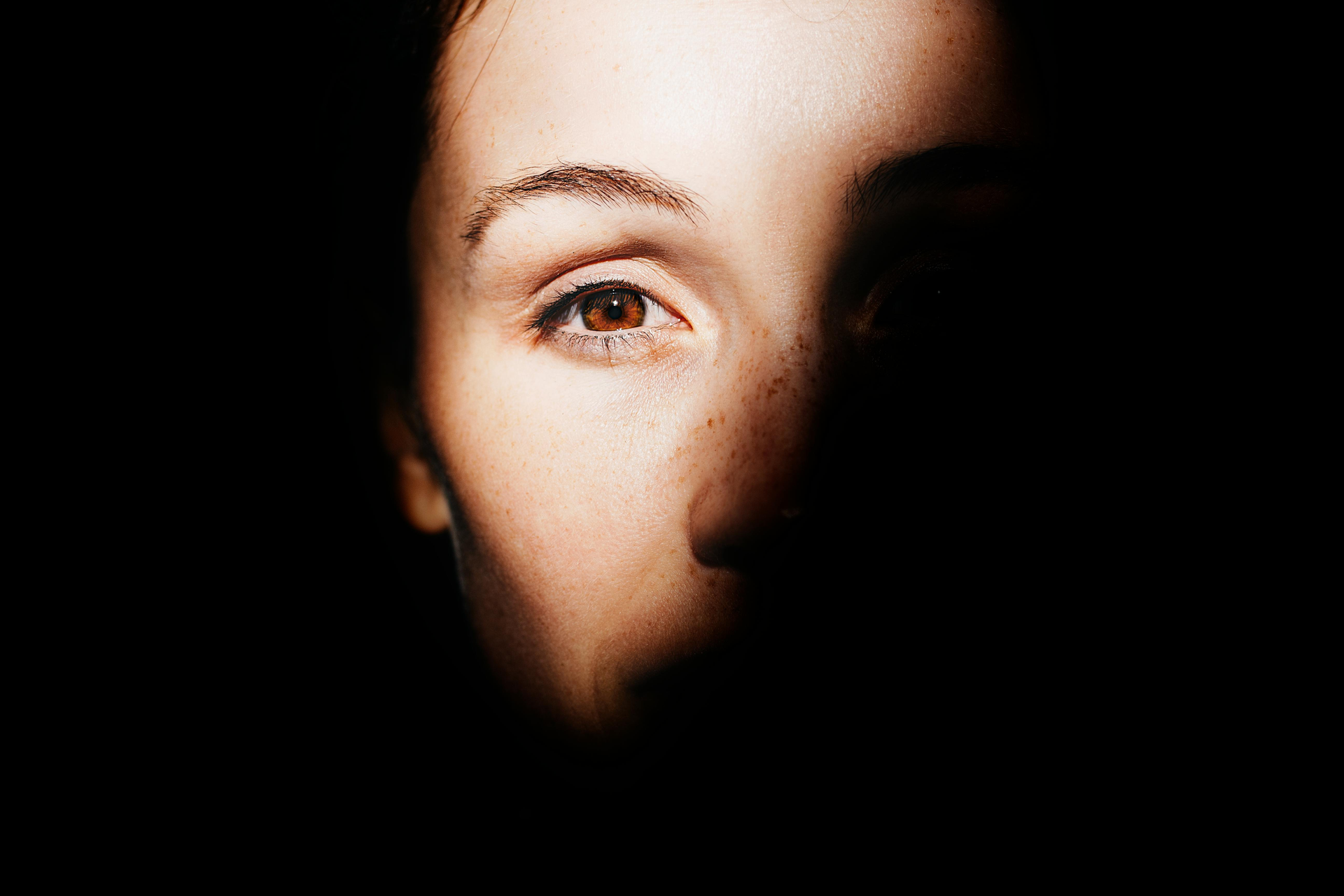 Close-up of a person's face in shadow, highlighting one brown eye, with a contemplative expression.