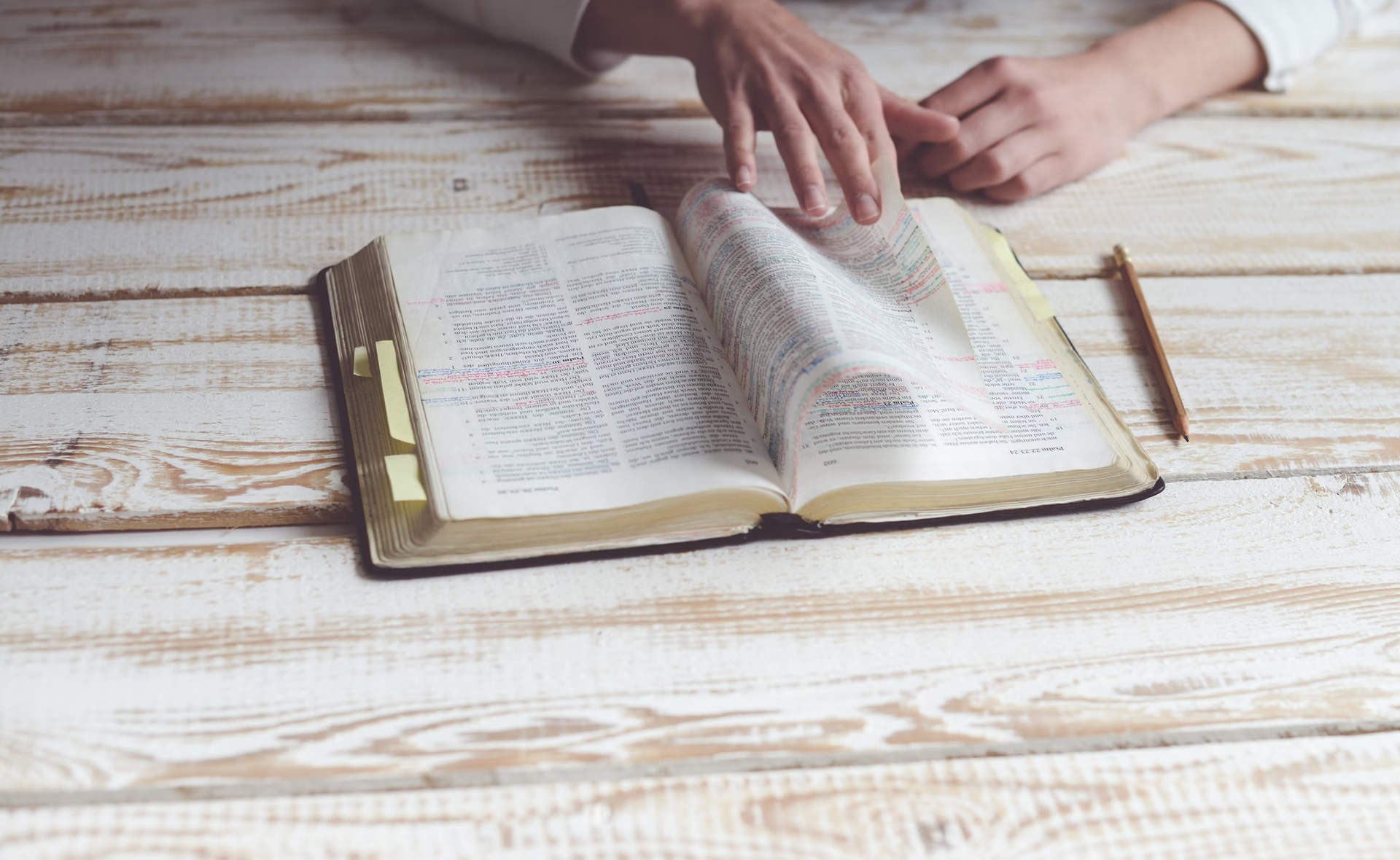 A person reading a bible on a wooden table.