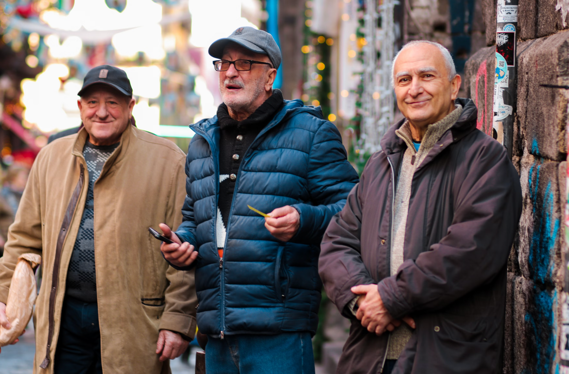 Three older men are standing next to each other on a city street.