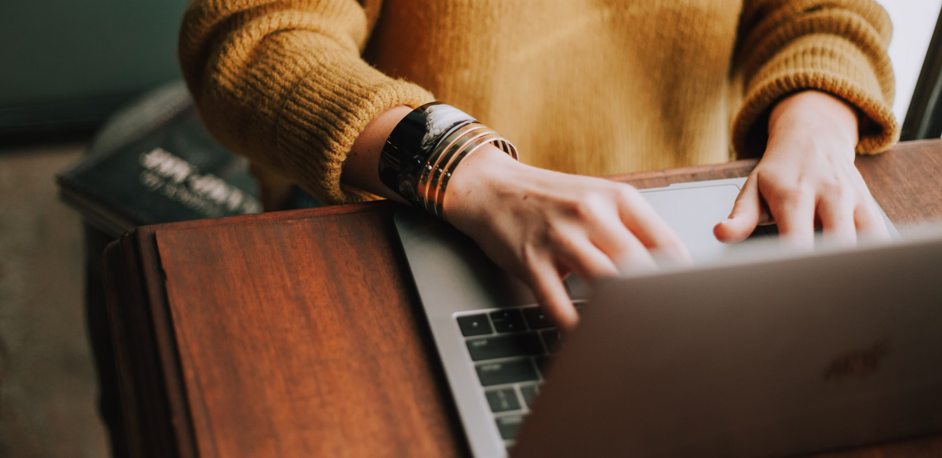 A woman in a yellow sweater is typing on a laptop computer for online missionary school.